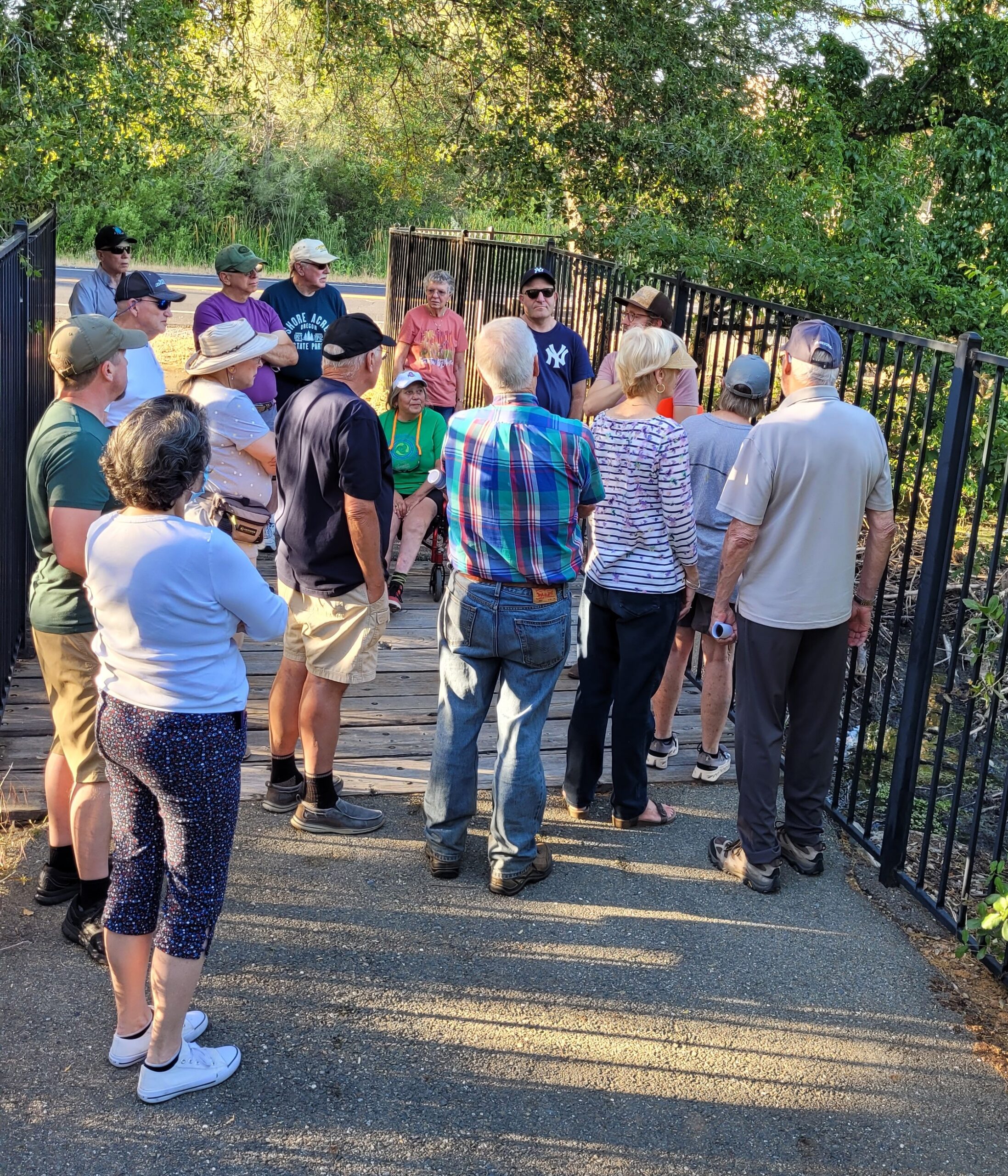 Community members on a bike path in a group listening to a speaker talk about beaver in a pond.